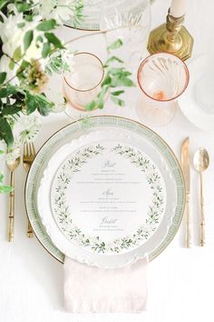 the table is set with plates, silverware and greenery on top of it