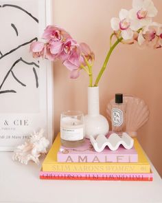 pink flowers are in a white vase next to some books and candles on a table