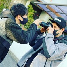 two young men wearing face masks and covering their faces with black cloths, taking pictures