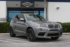 a silver bmw suv parked in front of a building with palm trees on the side