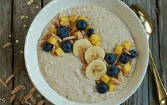 a white bowl filled with oatmeal topped with bananas and blueberries next to a spoon