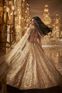 a woman in a gold gown with long hair standing next to a chandelier