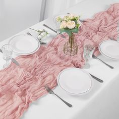 the table is set with white plates and silverware, pink ruffled tablecloth