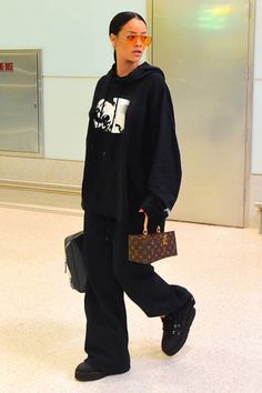 a woman walking through an airport carrying a suitcase and wearing a black hoodie with the word louis vuitton on it