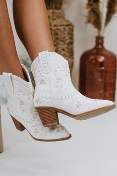 a woman wearing white cowboy boots standing on top of a wooden block heeled shoe