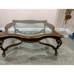 a coffee table with glass top and gold trimmings on the bottom, sitting on carpeted floor