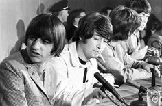 the beatles are sitting at a table with microphones in front of them and listening to someone else