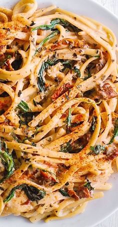 a white plate topped with pasta covered in sauce and spinach leafy toppings