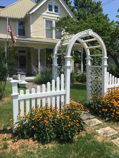 a white picket fence in front of a house with yellow flowers and an american flag