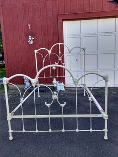 a white metal bed frame sitting in front of a red building with a garage door