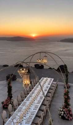 a long table set up with plates and silverware in front of the ocean at sunset