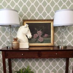 a table with two lamps and a painting on the wall in front of it next to a potted plant