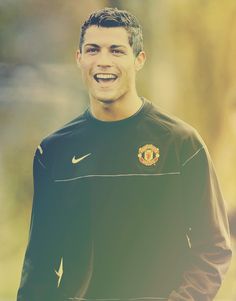 a young man is smiling and wearing a black shirt with the manchester united crest on it