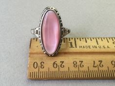 "It is difficult to tell just who made this ring. No legible makers mark but is stamped 925. Beautifully mounted. The cast silver pattern is nicely detailed and goes well with the mother of pearl. Pierced split band. Scintillating pink color. 1980s Design is 1 1/8\" long by 5/8\" wide 6.2 grams wt. Size 6.25 Attention: All items are listed to the best of our observation, but they are pre-owned and pre-loved (meaning we may have missed something minor and/or be in need of light cleaning.) Please Pink Sterling Silver Opal Ring For Anniversary, Pink Opal Ring In Sterling Silver For Anniversary, Pink Moonstone Sterling Silver Ring For Anniversary, Vintage Pink Cabochon Ring, Vintage Pink Hallmarked Rings, Classic Pink Cabochon Rings, Pink Oval Opal Ring In Sterling Silver, Pink Oval Moonstone Ring In Sterling Silver, Formal Pink Oval Opal Ring