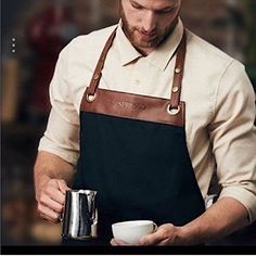 a man in an apron is holding a cup and looking down at his coffee mug