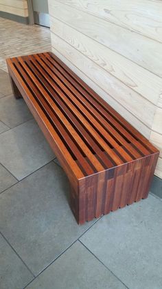 a wooden bench sitting on top of a tile floor next to a wall with wood slats