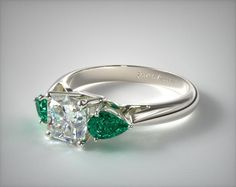 an emerald and diamond engagement ring on a white surface with the center stone surrounded by two pears