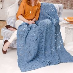 a woman sitting in a chair with a blue crocheted blanket