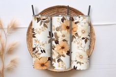 three floral tumbles sitting on top of a wicker basket next to some dry grass