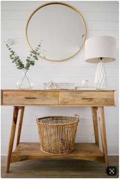 a wooden table topped with a basket under a mirror next to a wall mounted round mirror