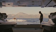 a man standing on the back of a boat looking out at the water and mountains