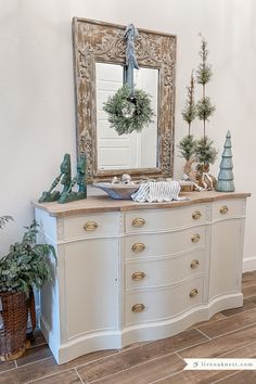 a white dresser topped with a mirror next to potted plants