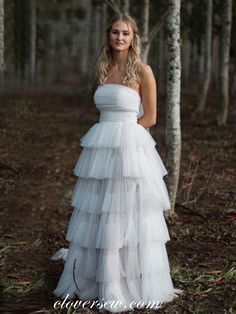 a woman standing in the woods wearing a white dress with ruffles on it