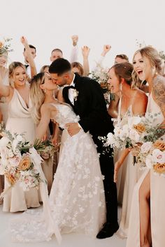 a bride and groom kissing surrounded by their bridal party guests in front of them