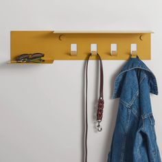 a coat rack with three hooks and two coats hanging from it's sides, next to a pair of jeans