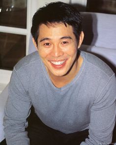 a man sitting on top of a white couch next to a window smiling at the camera