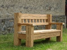 a wooden bench sitting in the grass next to a stone wall