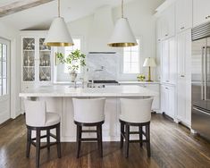 a kitchen with white cabinets and counter tops, three stools in front of the island