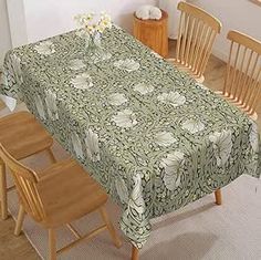 a dining room table covered with a green and white flowered tablecloth next to wooden chairs