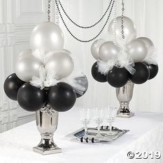 two silver and black balloons are on a white table cloth with candles in front of them