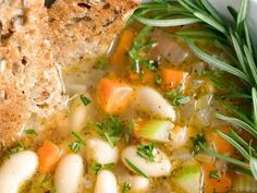 a white bowl filled with soup next to a piece of bread and green garnish