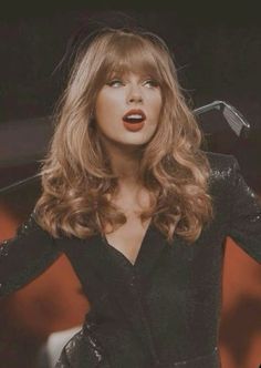 taylor swift is wearing a black dress with sequins on the sleeves and her hair blowing in the wind