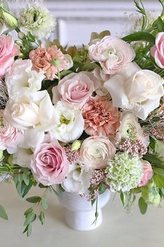 a white vase filled with lots of pink and white flowers on top of a table