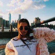 a woman wearing sunglasses and holding a teddy bear in front of a cityscape