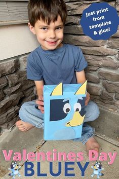 a young boy sitting on the ground holding up a blue box with an image of a dog