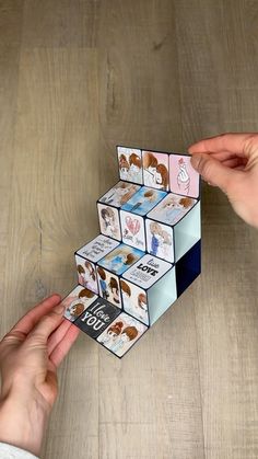 two hands are holding an origami box with pictures on it and one hand is reaching for the other