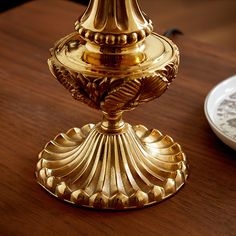 a golden candle holder sitting on top of a wooden table next to a white plate