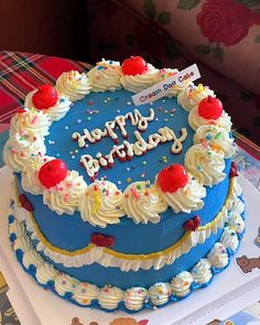 a blue birthday cake with white frosting and red cherries on top is sitting on a table