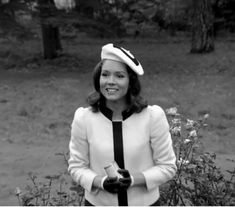 black and white photograph of a woman wearing a hat and tie with flowers in the background