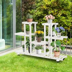 a white shelf with potted plants on it in front of a glass wall and green grass