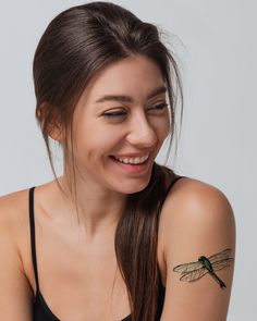 a woman with a dragonfly tattoo on her arm smiling and looking at the camera