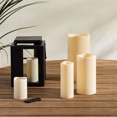 three white candles sitting on top of a wooden table next to a cell phone and remote control