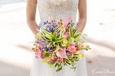 a bride holding a bouquet of flowers on the beach