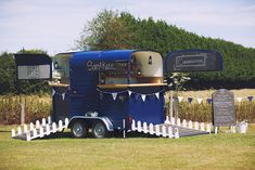 a blue trailer parked on top of a lush green field next to a white picket fence