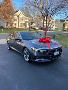 a gray car with a red bow on the hood parked in front of a house