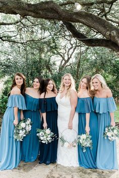 the bridesmaids in blue dresses are posing for a photo under a large tree